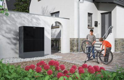 Wärmepumpe von Viessmann vor einem Wohnhaus, während zwei Kinder ein Fahrrad reparieren